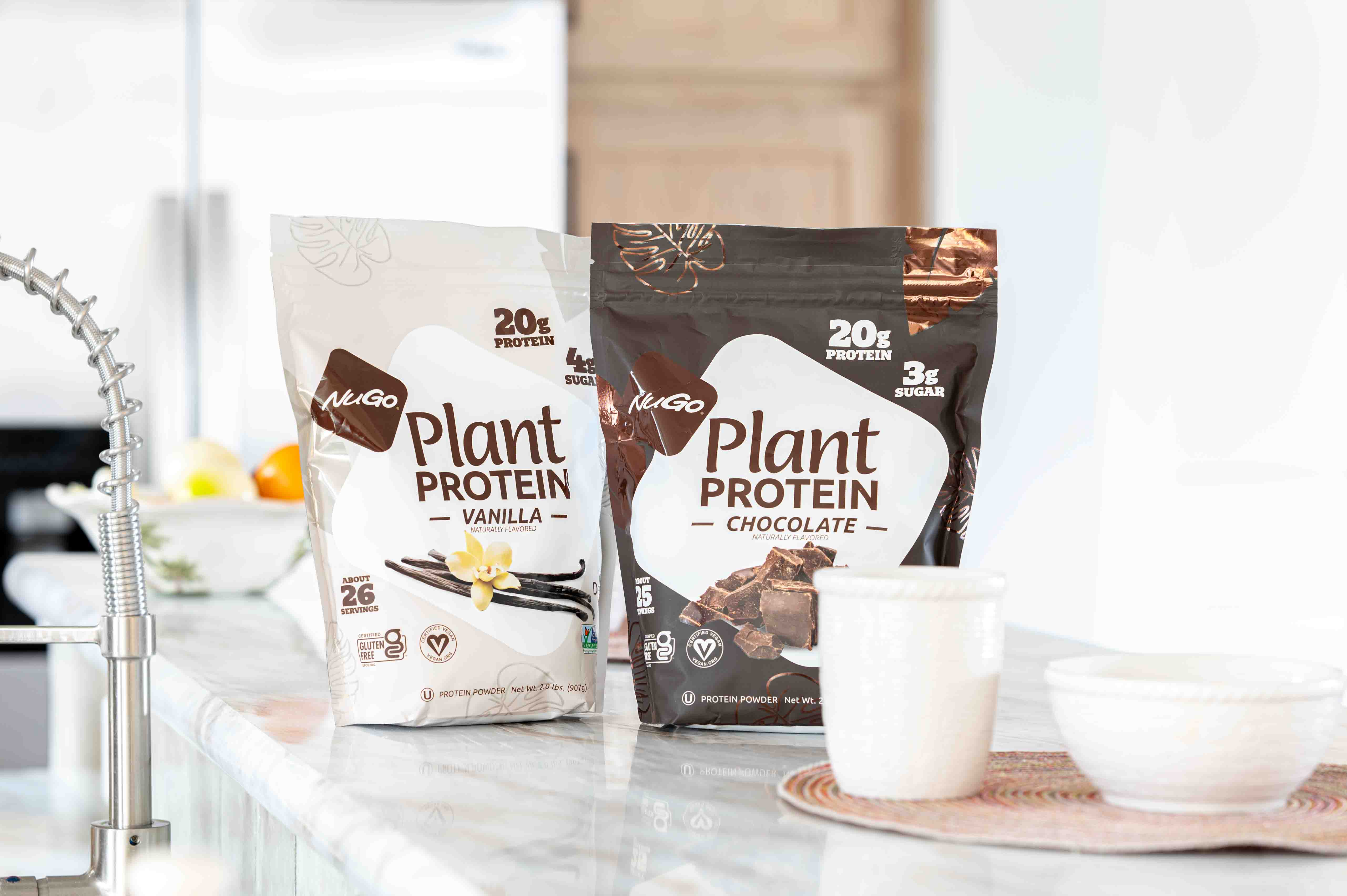 A bag of Vanilla and a bag of Chocolate NuGo Protein Powder on a marble counter top