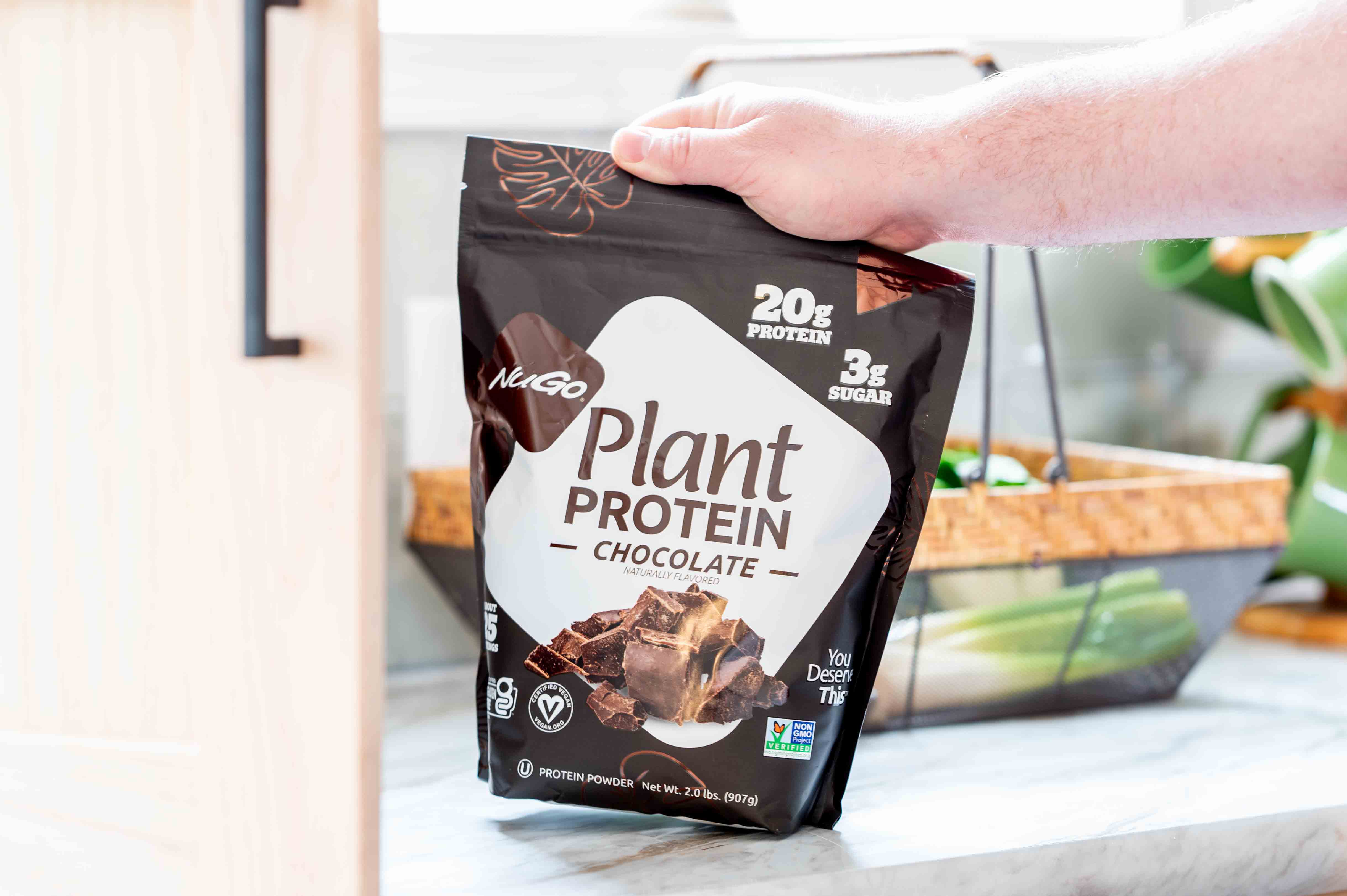 A bag of Chocoalte NuGo Protein Powder in front of a basket of vegetables