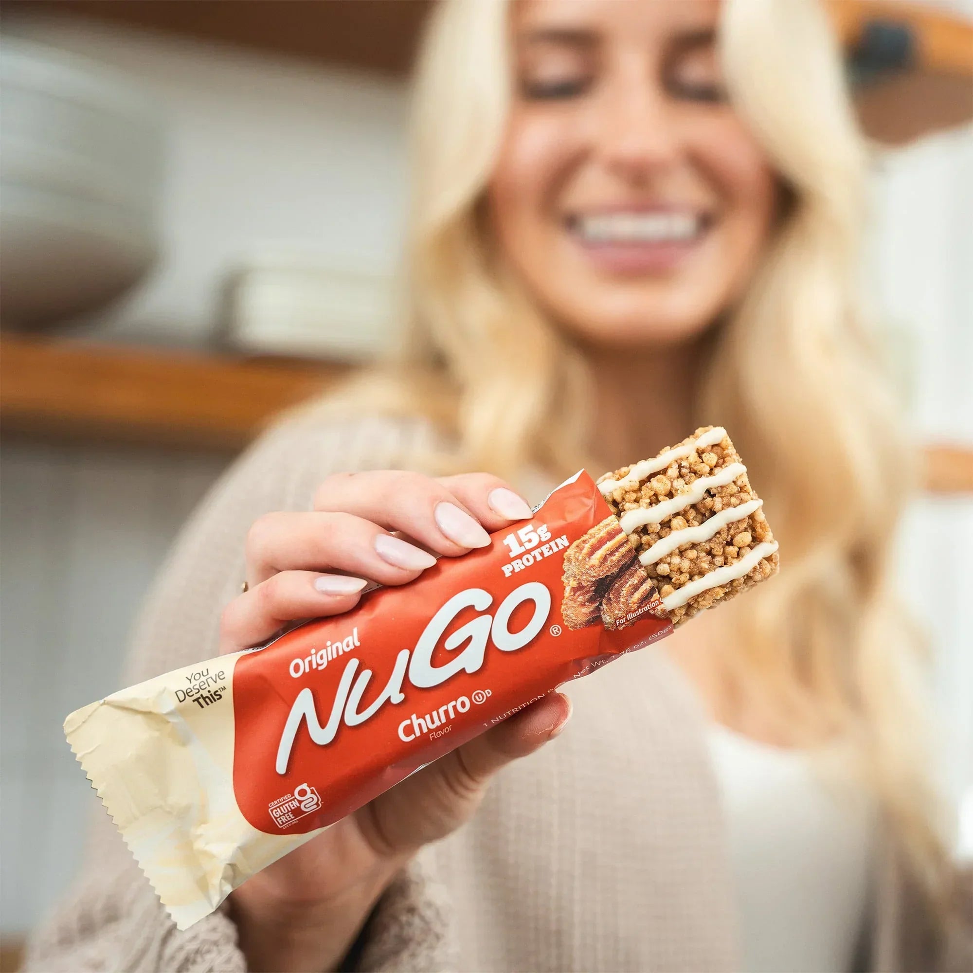 Woman holding a NuGo Churro protein bar with a blurred background