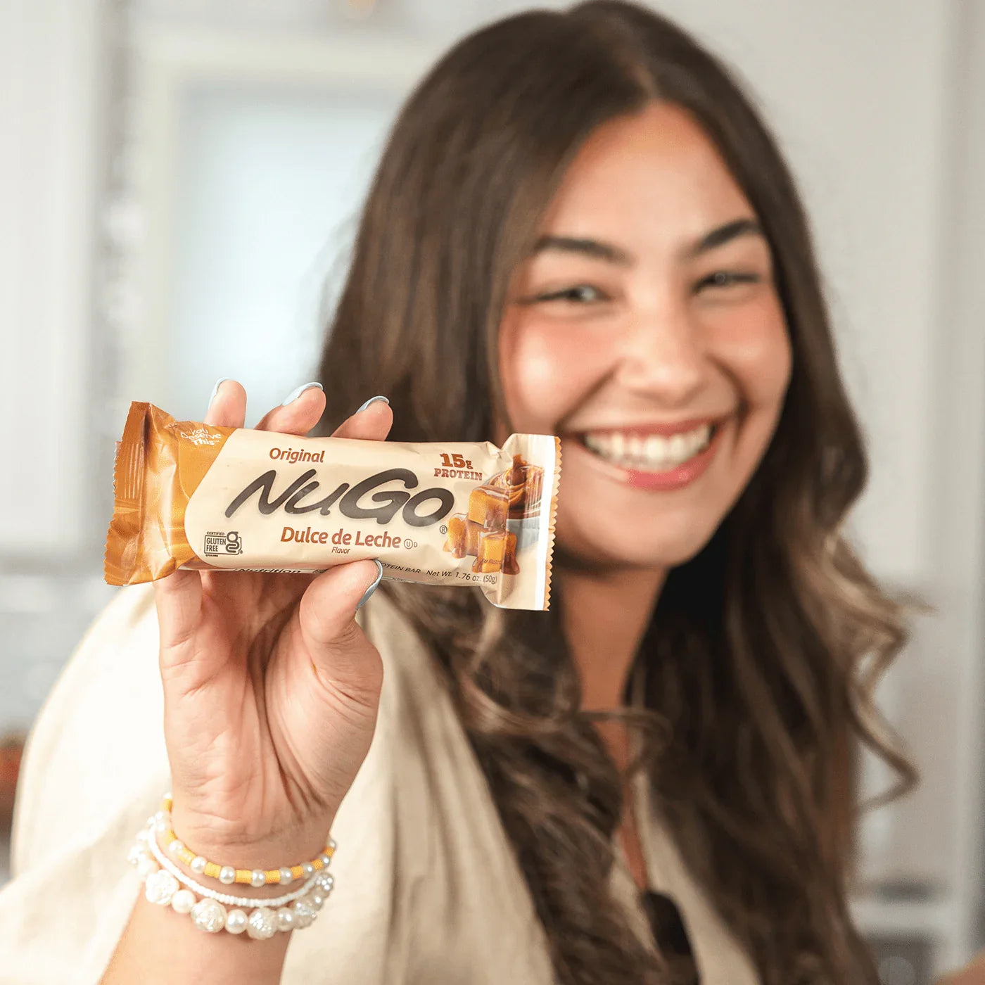 Woman holding a NuGo Dulce de Leche bar and smiling