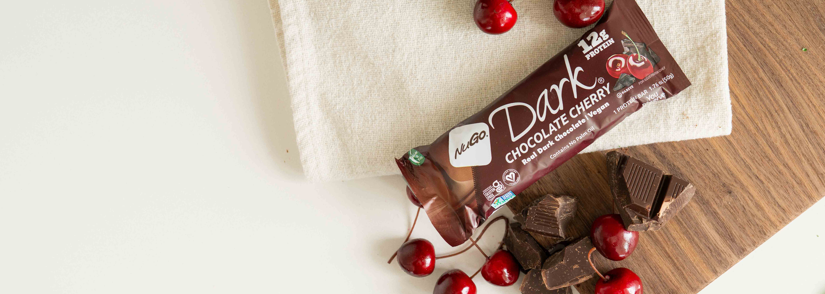NuGo Dark Chocolate Cherry Bar on cutting board with chocolate and cherry ingredients.