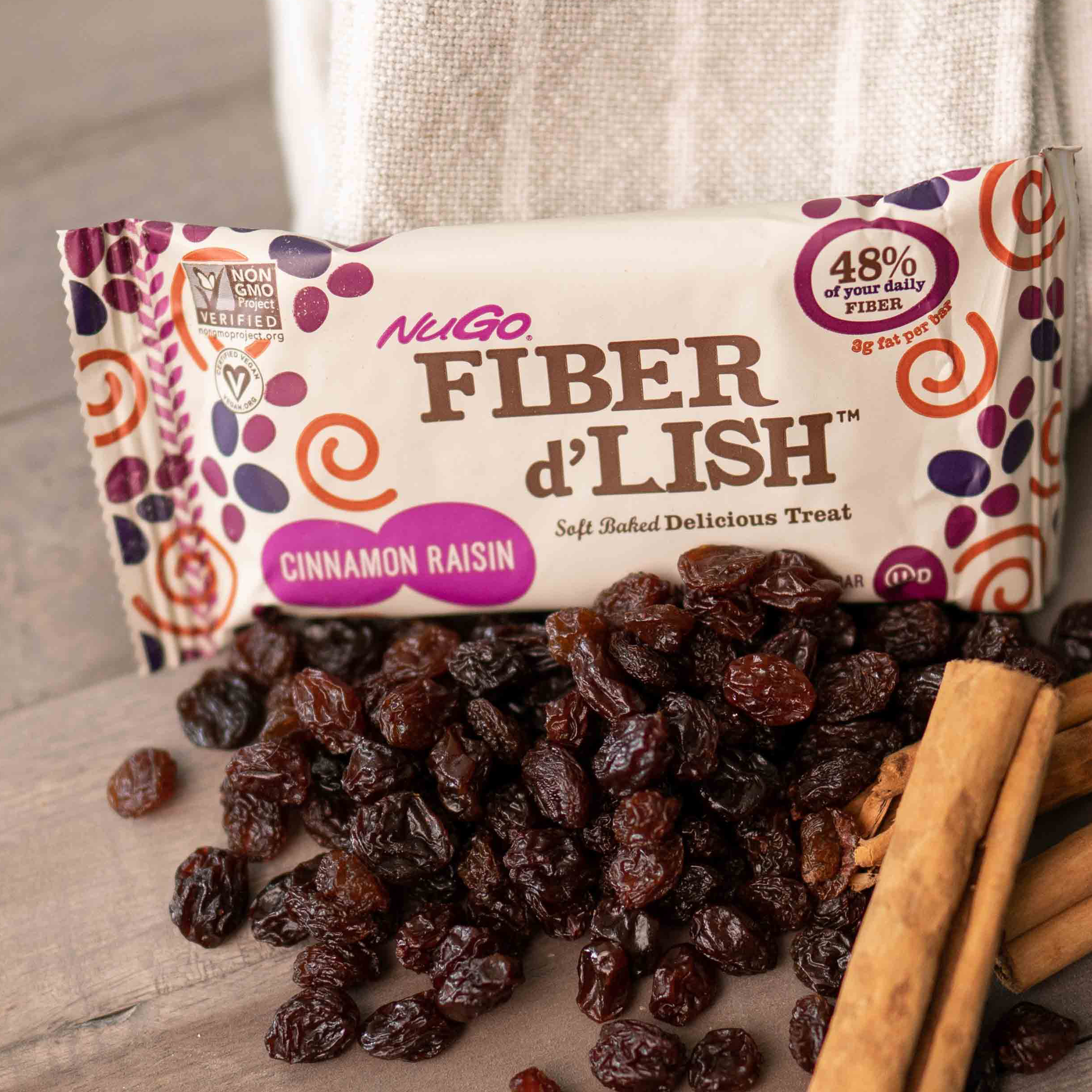NuGo Fiber Cinnamon Raisin Wrapped bar with a pile of Raisins next to it