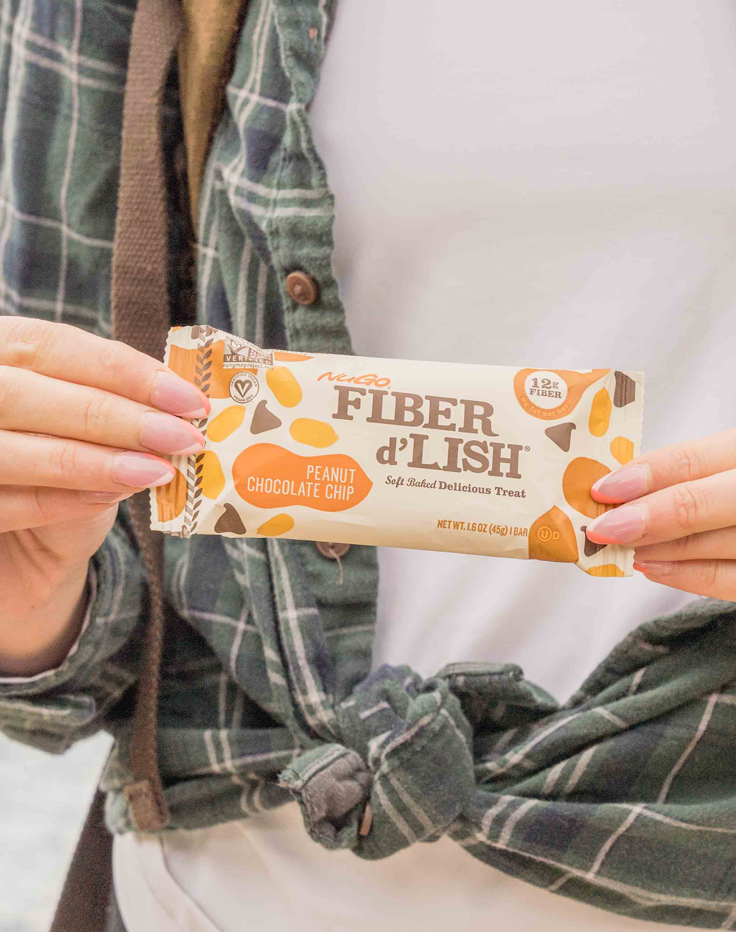 Woman, outisde, hold NuGo Fiber Peanut Chocolate Chip bar in front of body