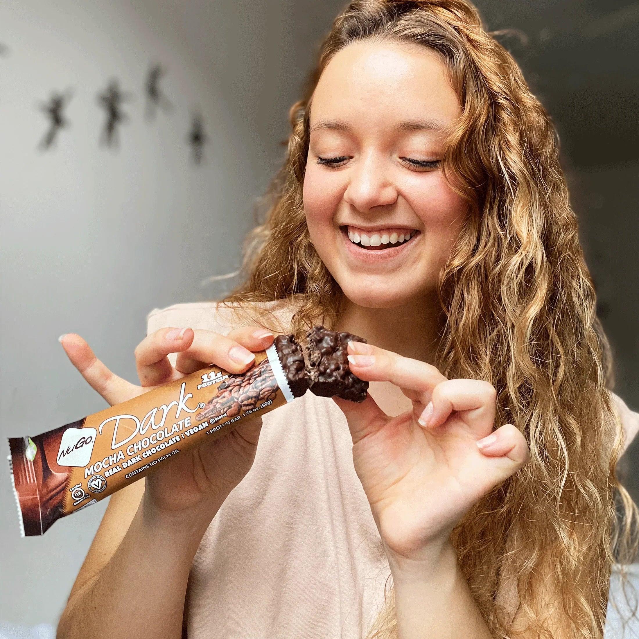 Woman holding a NuGo Dark Mocha Chocolate bar, smiling.