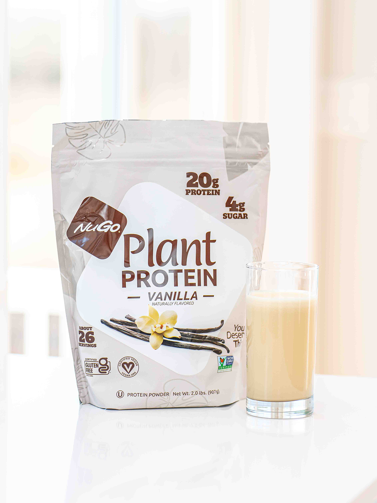 A bag of Vanilla NuGo Protein Powder next to a tall glass of the mix