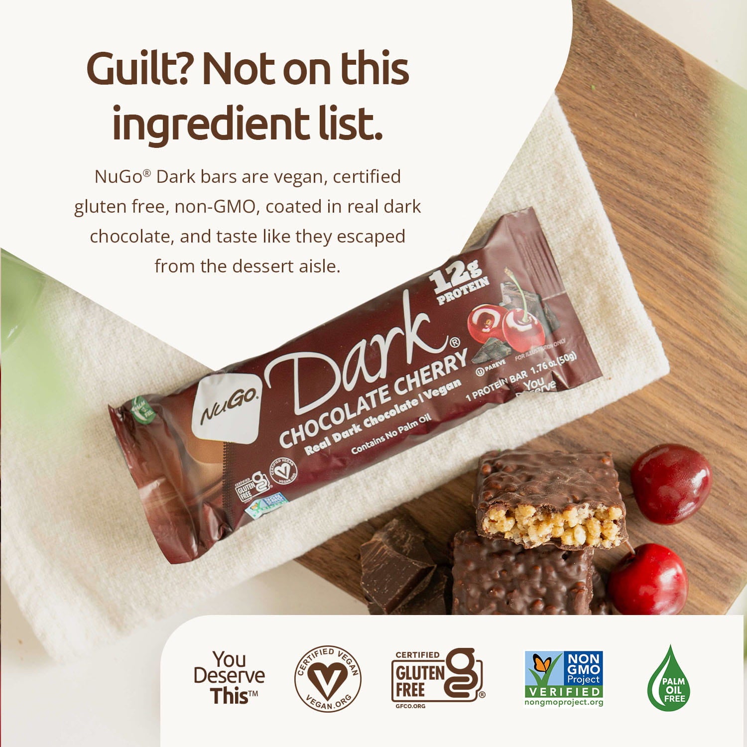 NuGo Dark Chocolate Cherry protein bar on a wooden surface with branding and certification logos.