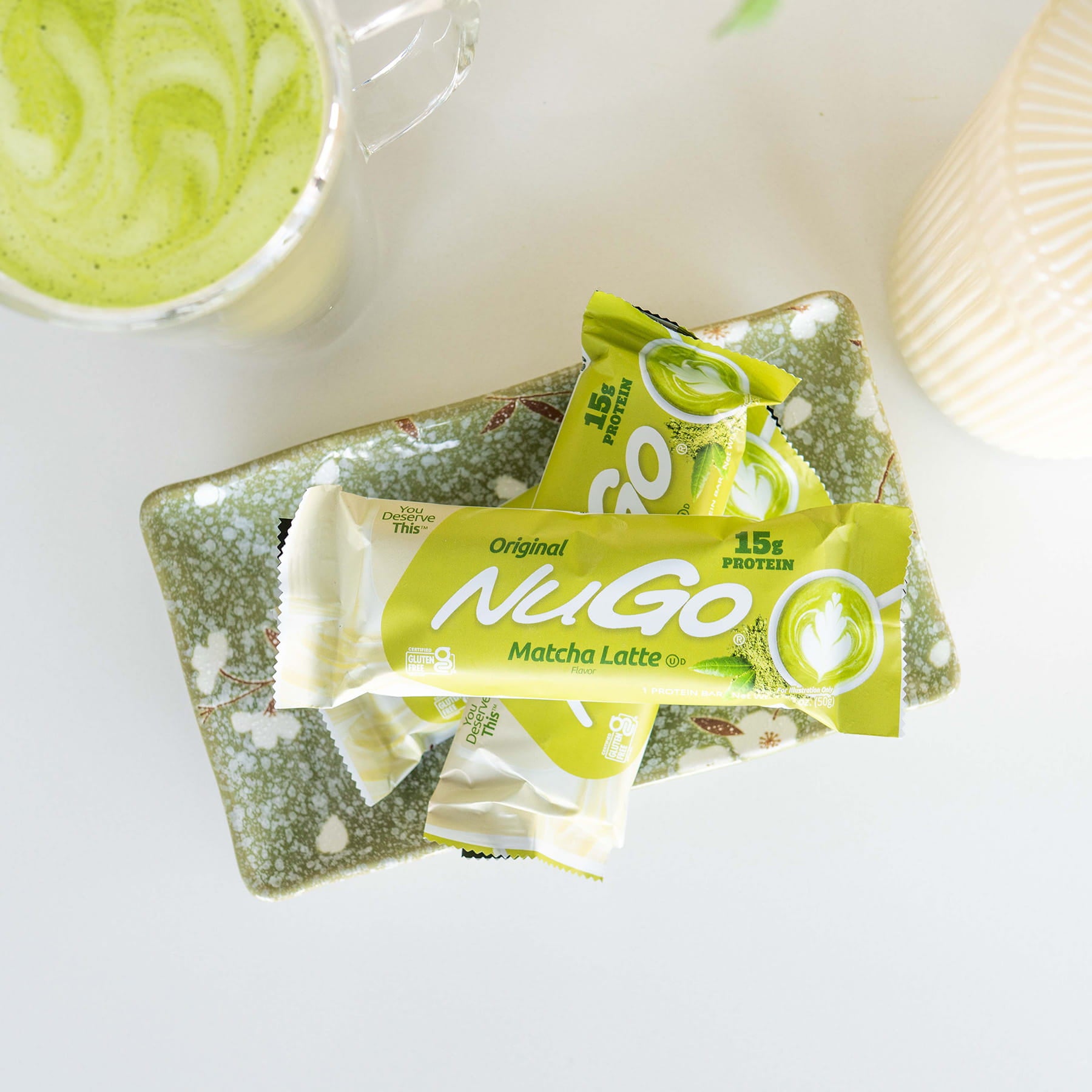 NuGo Matcha Latte protein bars on a white surface with a cup of matcha latte in the background.
