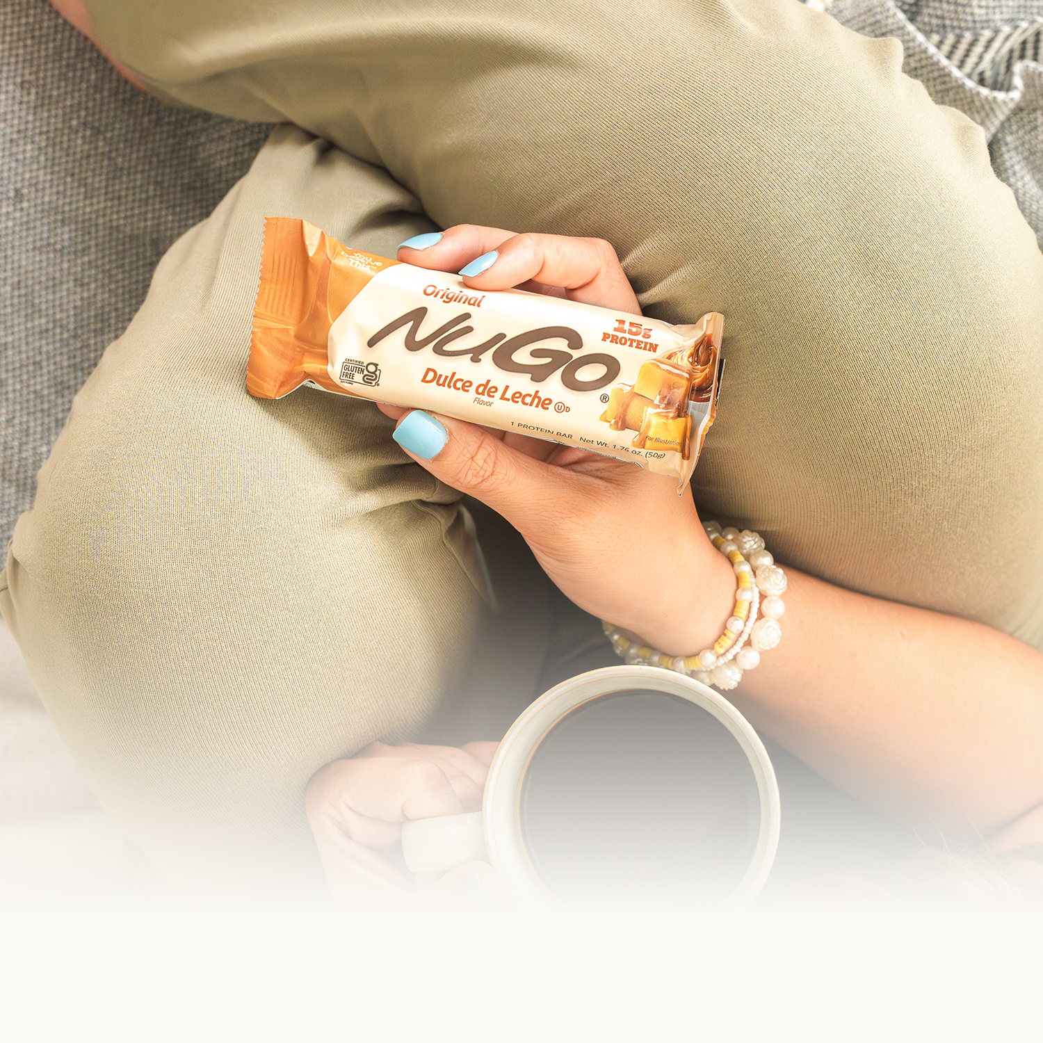 NuGo Original bar being held in lap with cup of coffee. 