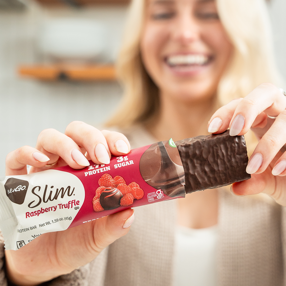Woman holding a Slim Raspberry Truffle protein bar with a blurred background